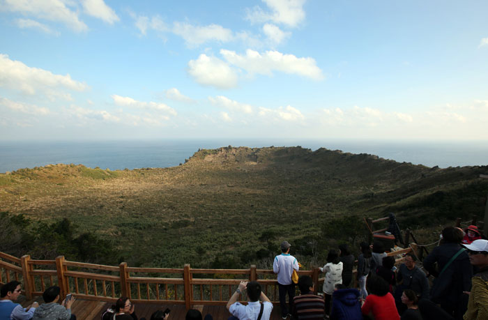 People on the Seongsan <i>Ilchulbong</i> take photos of the scenic view. From the top, they can see the wide open bowl of the crater, looking like an expanse of grassland. 