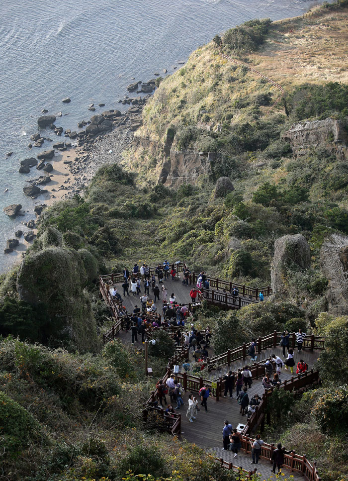 People appreciate the surrounding view of the Seongsan <i>Ilchulbong</i>, while resting during their climb to the top.