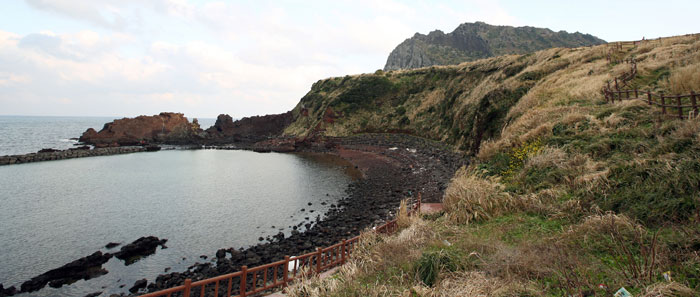 The ocean view can be seen on the right while descending the Seongsan <i>Ilchulbong</i>. This beach has black sand, which can be found scattered around the beaches of Jeju.